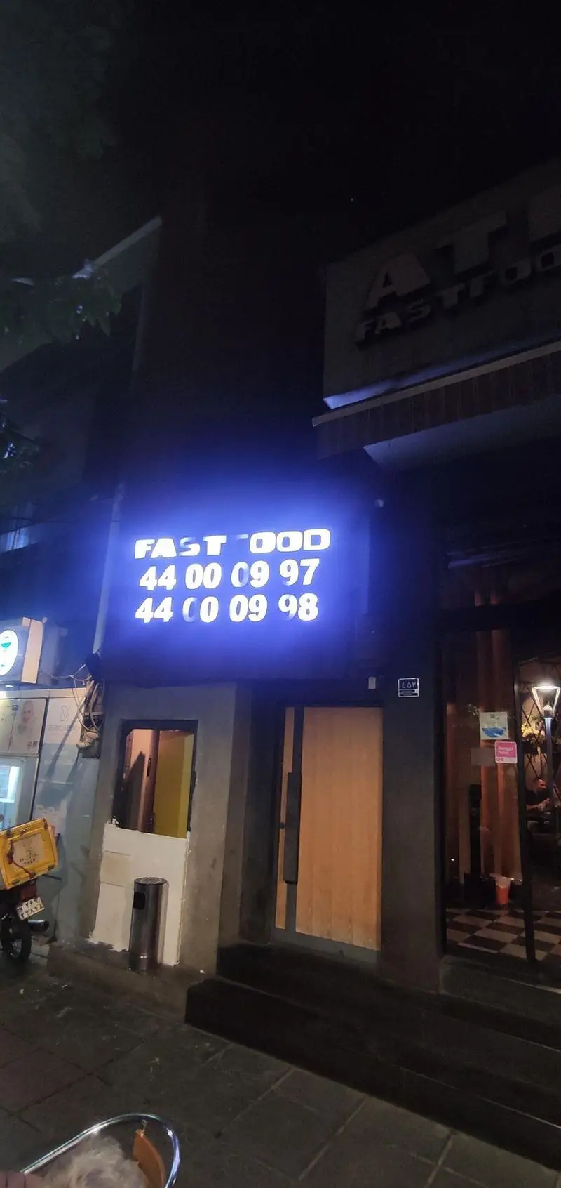 تصویر شبانه از نمای بیرونی فست فود ای تی اف شعبه کاشانی با تابلوی نئونی روشن و شماره تلفن‌های 44000997 و 44000998 جهت سفارش.