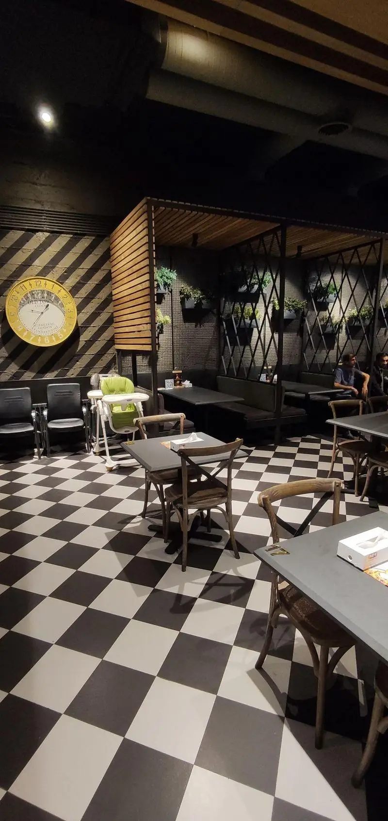 فضای داخلی دنج کافه رستوران ای تی اف شعبه کاشانی؛ کف شطرنجی، میز و صندلی چوبی، دیوار با ساعت و گیاهان آویز، مناسب برای خانواده.