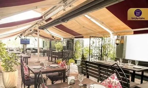 فضای باز دلنشین رستوران توتیا با میز و صندلی‌های چوبی، آلاچیق‌های سایبان‌دار، گیاهان سرسبز و محیطی آرامش‌بخش برای مشتریان.