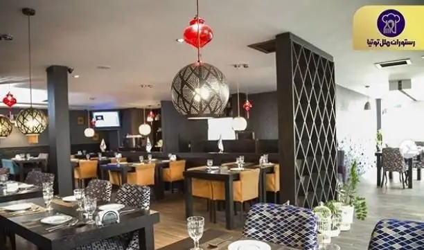 دکوراسیون داخلی لوکس و مدرن رستوران توتیا با میز و صندلی‌های شیک، لوسترهای خاص و فضایی گرم و صمیمی برای تجربه غذایی لذت‌بخش.