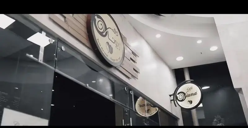 ورودی مدرن کافه ویونا با تابلوی دایره‌ای شکل شامل لوگوی قهوه و نام کافه به فارسی و انگلیسی، آماده استقبال از مشتریان.