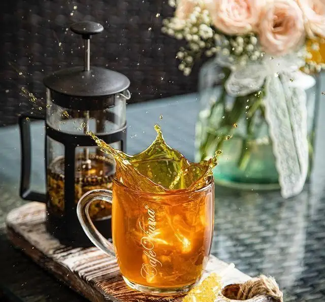 نوشیدنی چای سرد کافه ویونا با اسپلش دیدنی در لیوان شفاف، در کنار فرنچ پرس و گل‌های زیبا؛ حس خنکی و طراوت.