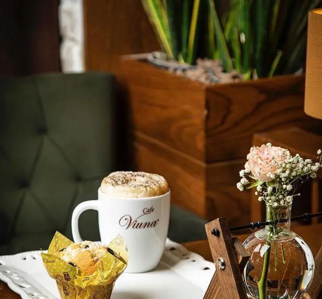 یک فنجان قهوه داغ کافه ویونا در کنار مافین تازه و گل‌های زیبا؛ ایده‌آل برای یک صبحانه یا عصرانه دلنشین در محیط دنج کافه ویونا.