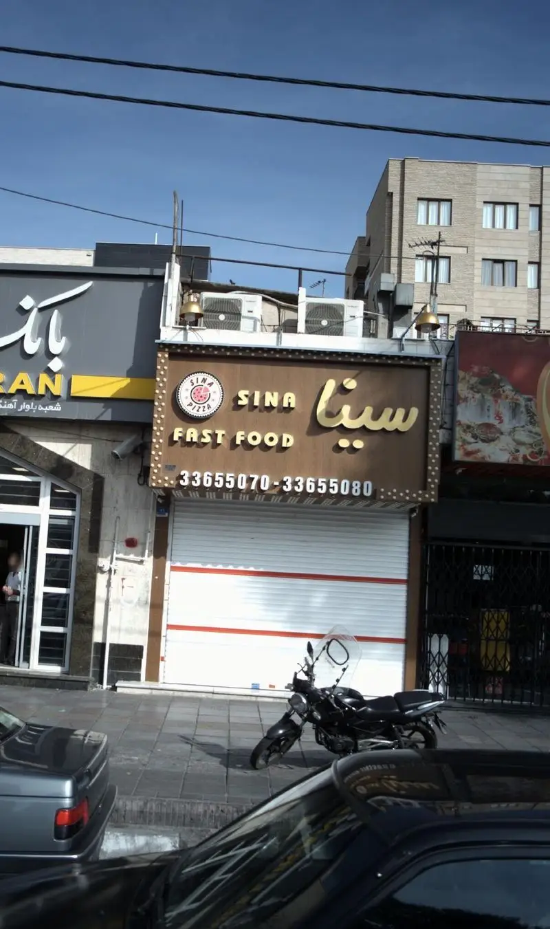 نمای بیرونی فست فود سینا با تابلوی طلایی و لوگوی پیتزا، شماره تماس 33655070 و 33655080 در تهران، مناسب برای سفارش غذاهای سریع.