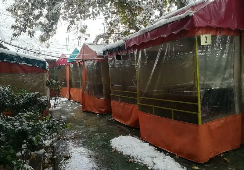 فضای باز رستوران سنتی اراج با آلاچیق‌های مجهز و گرم در روز برفی زمستان، مکانی ایده‌آل برای تجربه غذایی دلچسب.