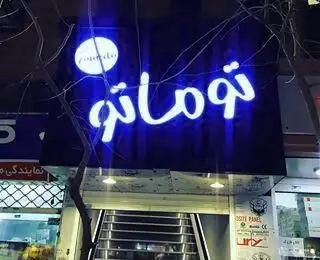 تابلوی نئون آبی‌رنگ و درخشان رستوران ایتالیایی توماتو در شب، با نمایش لوگو و نام "توماتو"، ورودی شیک آن را روشن کرده است.