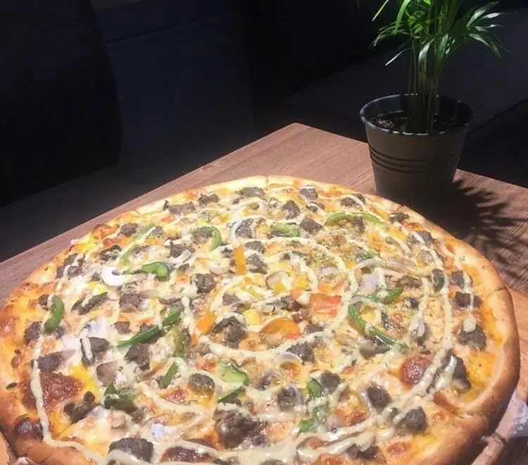 پیتزای بزرگ و پرملات گوشت و سبزیجات (فلفل، پیاز) رستوران ایتالیایی توماتو با سس مخصوص، روی میز چوبی در محیط دنج.