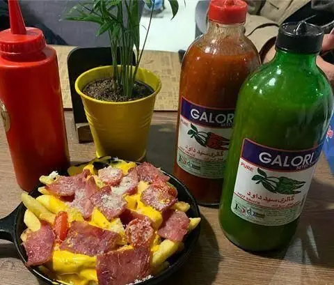 سیب زمینی سرخ کرده خوشمزه با پنیر چدار آب شده و برش‌های سوسیس، همراه سس‌های تند گالوری در رستوران ایتالیایی توماتو.