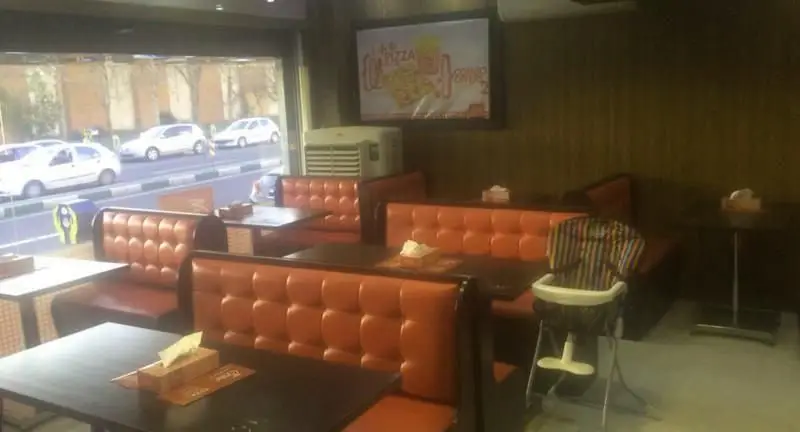 فضای داخلی رستوران فست فود عطاویچ اکباتان با چیدمان میز و صندلی‌های نارنجی، پنجره بزرگ رو به خیابان و محیطی دنج و خانوادگی.