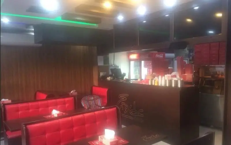 نمایی از محیط دلنشین و مدرن فست‌فود عطاویچ اکباتان، با چیدمان صندلی‌های قرمز راحتی و کانتر مجهز به تجهیزات آماده‌سازی غذا.