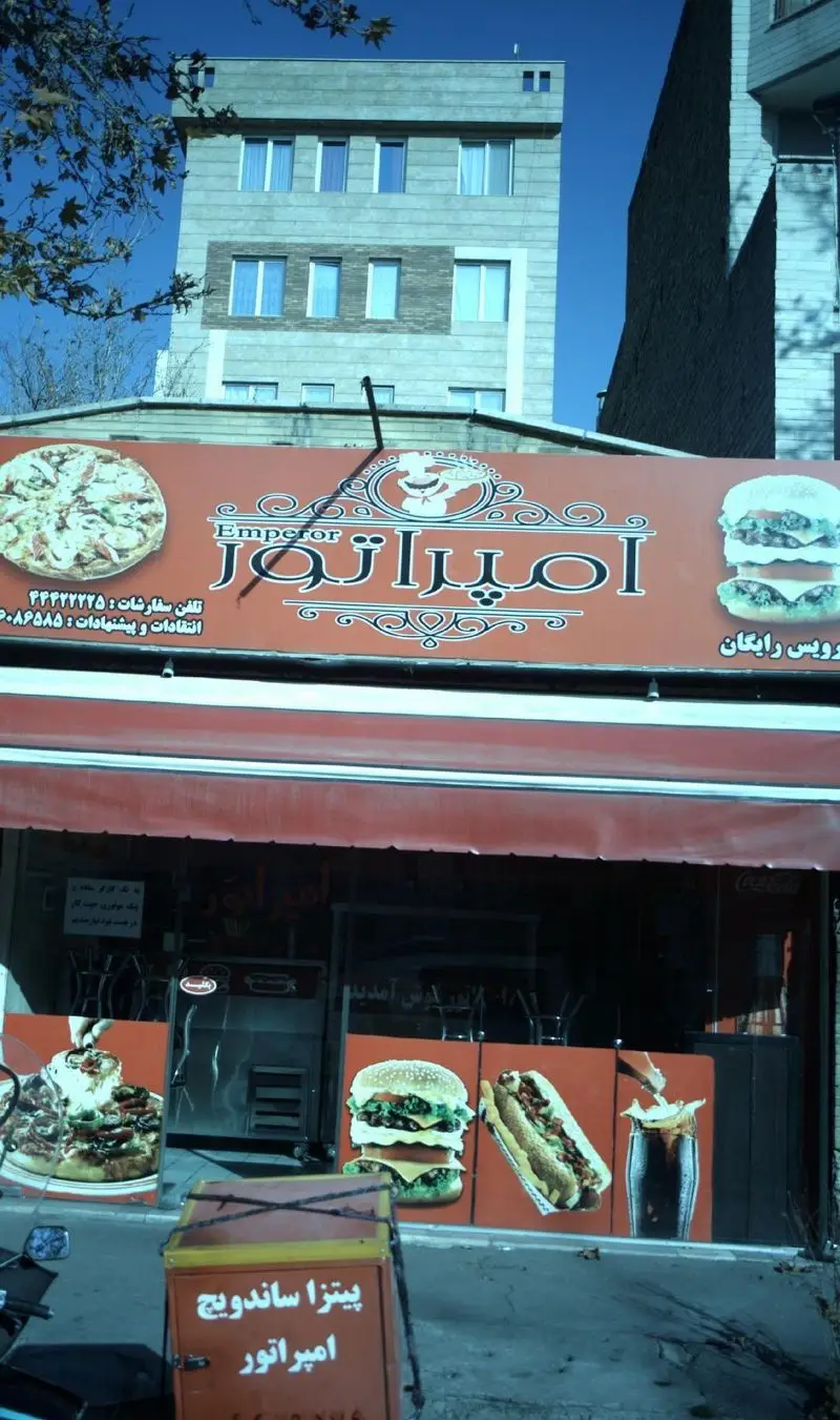مغازه پیتزا و ساندویچ امپراتور، فست فود با تابلوی بزرگ حاوی عکس پیتزا، همبرگر و ساندویچ. آماده برای سفارش و دلیوری.