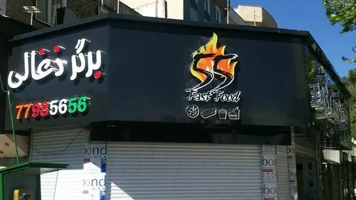 نمای بیرونی فست فود 55 برگر ذغالی با لوگوی شعله، شماره تلفن 77985656 و نمادهای پیتزا، هات داگ و سیب‌زمینی سرخ‌کرده