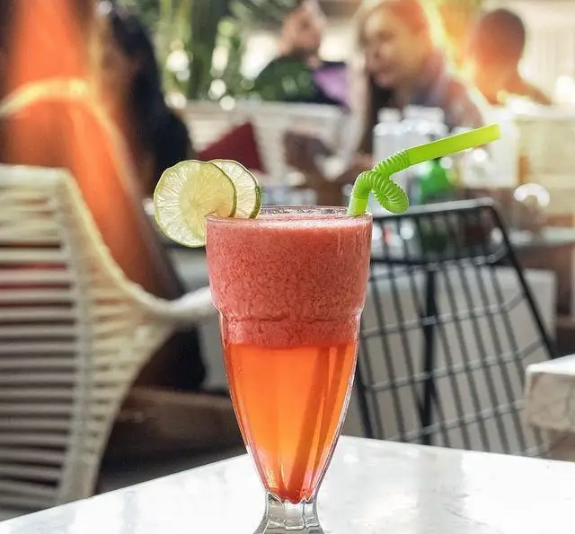تصویری دلنشین از کافه رستوران کالوک: یک نوشیدنی اسموتی دو رنگ (قرمز و نارنجی) با تزیین لیمو و نی سبز روی میز.