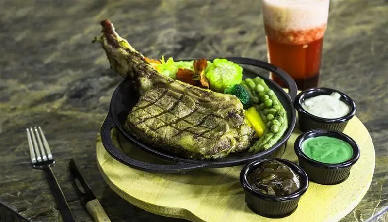 استیک توماهوک آبدار با سبزیجات گریل شده، سس‌های متنوع و نوشیدنی مخصوص در کافه رستوران کالوک، یک غذای لذیذ و کامل.