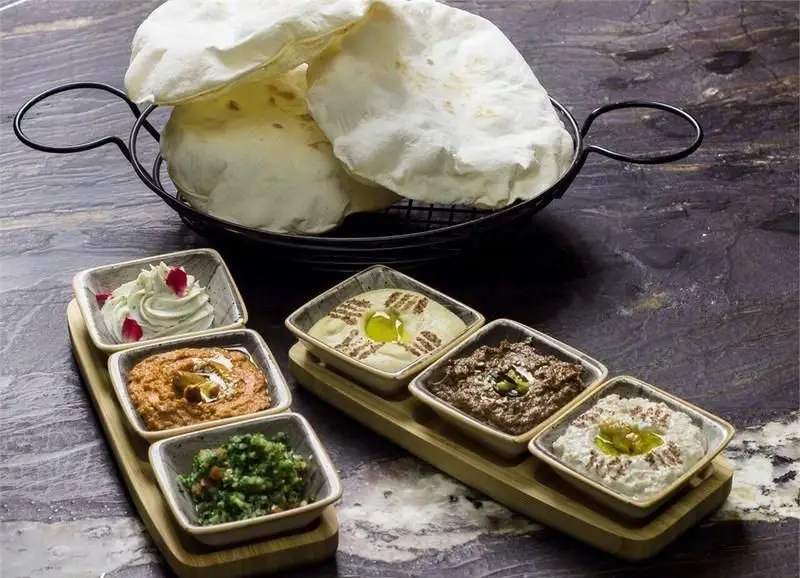 پیش غذاهای متنوع و خوشمزه کافه رستوران کالوک شامل حمص، باباغنوش، تبوله، لبنه و نان پیتا تازه در یک میز زیبا برای مشتریان