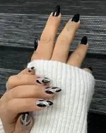 طراحی ناخن اسپرت مشکی و نقره‌ای با طرح‌های شعله‌ای و مینیمال شیک روی ناخن‌های بلند بادامی همراه با آستین بافتنی سفید زنانه
