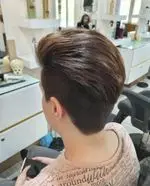 نمای نزدیک از مدل موی زنانه کوتاه و شیک با فرق کج و هایلایت‌های بلوند در سالن زیبایی طرفه.