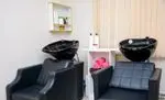 سالن زیبایی همتا: دو صندلی مدرن و دو سینک مشکی مدرن برای خدمات شستشوی مو و آرایشگاه در فضایی دلنشین.