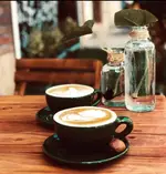 دو فنجان قهوه لاته با طرح هنری زیبا روی میز چوبی کافه آربا. لذت یک نوشیدنی گرم در فضای دلنشین و آرامش‌بخش.