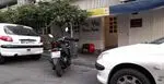 نمای بیرونی پیتزا پاشا، فست فود معروف، در خیابان با خودروی سفید و موتور سیکلت پارک شده و جعبه تحویل غذا.
