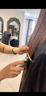 آرایشگر ماهر در سالن زیبایی آزیتا امیری در حال کوتاهی و اصلاح دقیق موی بلند مشتری با دستگاه موزن و شانه، تجربه‌ای دلپذیر.
