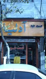 تصویر نمای بیرونی فست فود آدلیا با تابلوی نارنجی، نمای خیابان، شماره تماس و درخت در پیش‌زمینه. ۴۴۰۱۷۴۹۸-۴۴۰۱۷۴۹۷