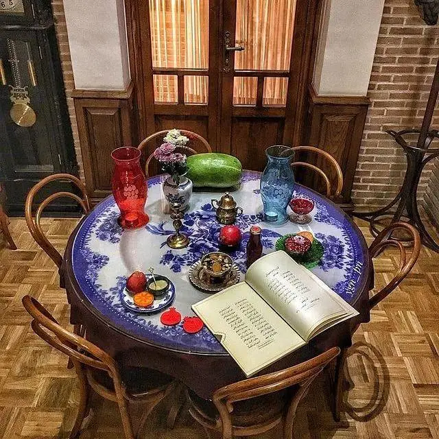 میز گرد سنتی کافه لقانطه با دکوراسیون دلنشین، شامل هندوانه، انار، گل، ظروف قدیمی و کتاب باز، فضایی نوستالژیک و جذاب.