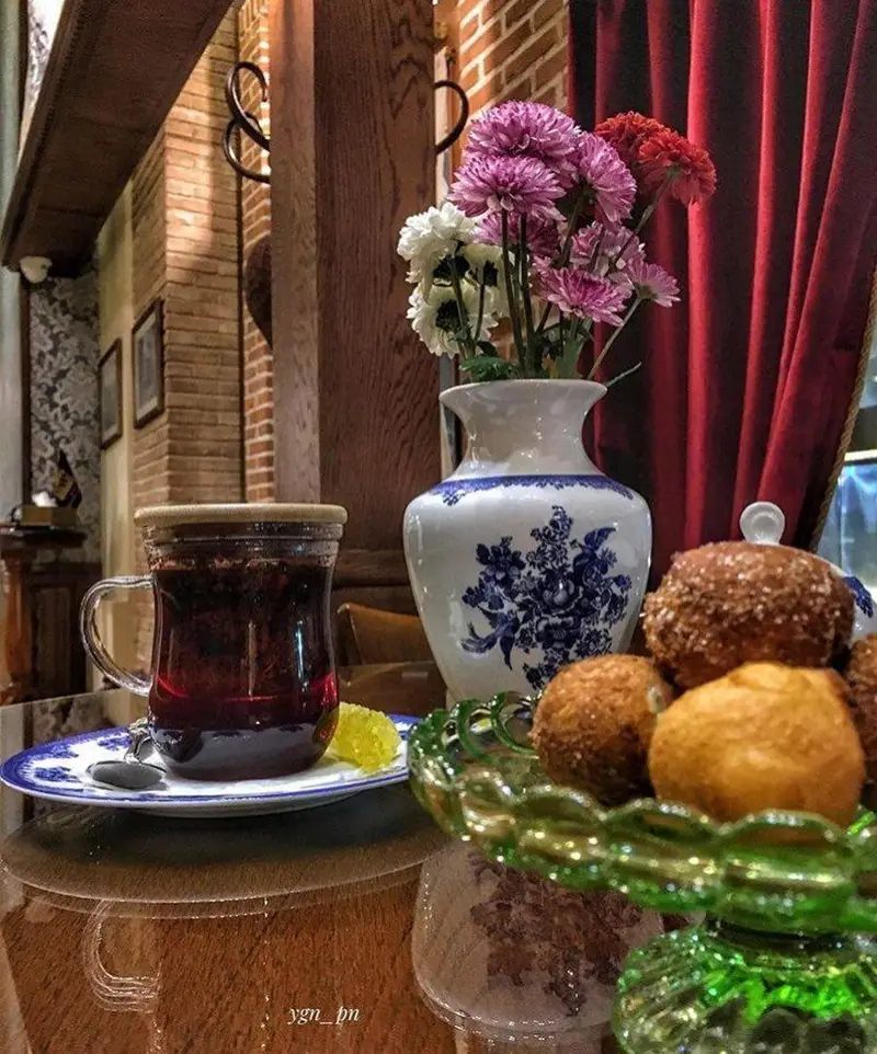 نمایی دلنشین از کافه لقانطه، شامل چای دمنوش خوشرنگ، گلدان گل و شیرینی‌های سنتی در فضایی گرم و دلپذیر برای تجربه ای خاص.