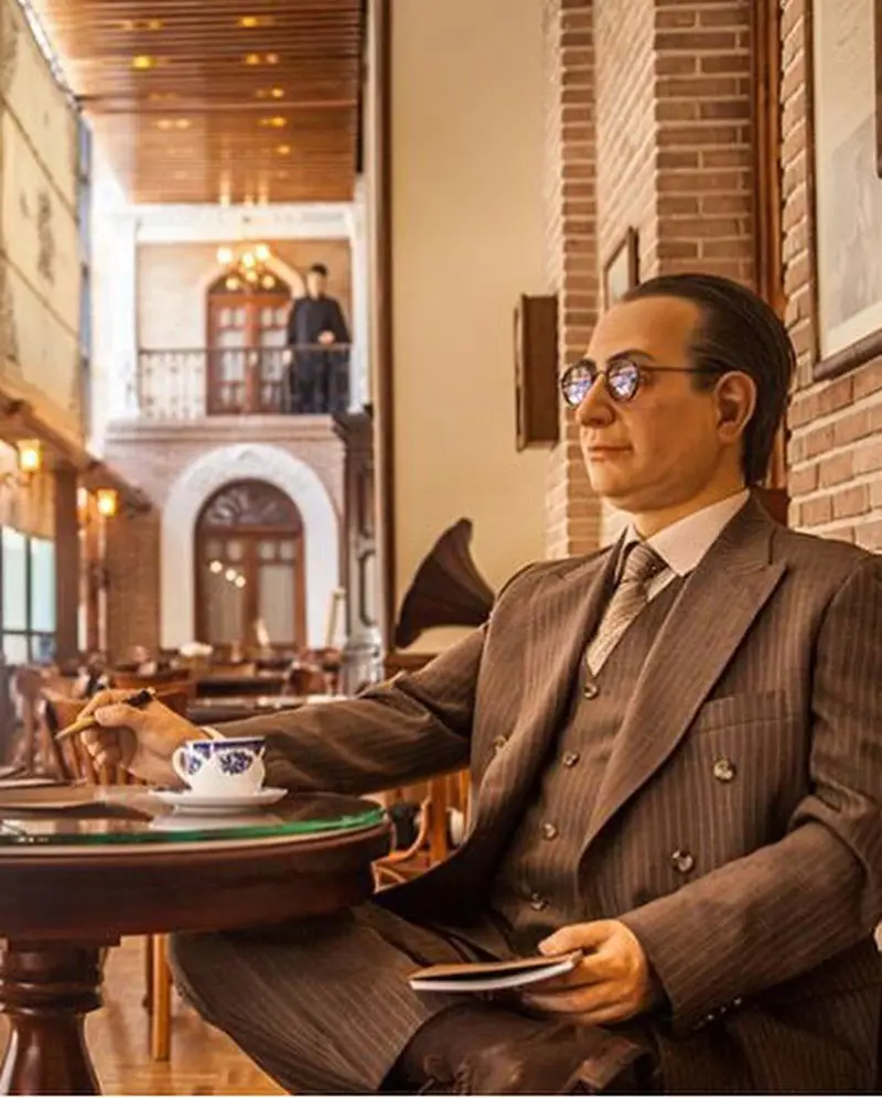 مجسمه مردی با عینک و کت و شلوار راه راه در حال نوشتن در کافه لقانطه، فضایی نوستالژیک برای لذت بردن از قهوه و چای.