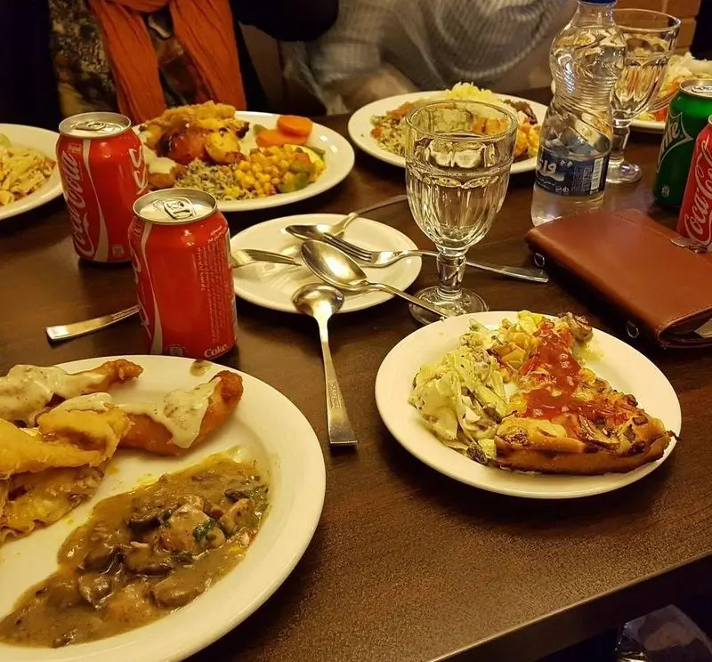 میز پر از غذاهای متنوع و لذیذ در رستوران ایرانی شهربانو، شامل پلو، مرغ، خوراک قارچ، پیتزا و نوشیدنی. تجربه‌ای دلپذیر از غذاهای باکیفیت.