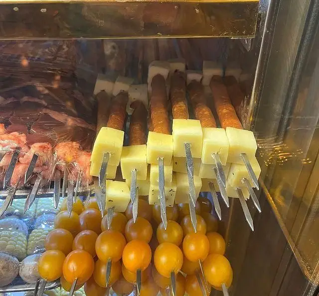 سیخ‌های متنوع کباب شامل سوسیس با پنیر، گوجه گیلاسی و گوشت‌های تازه در ویترین جگر ذغالی پامچال، آماده برای پخت ذغالی.