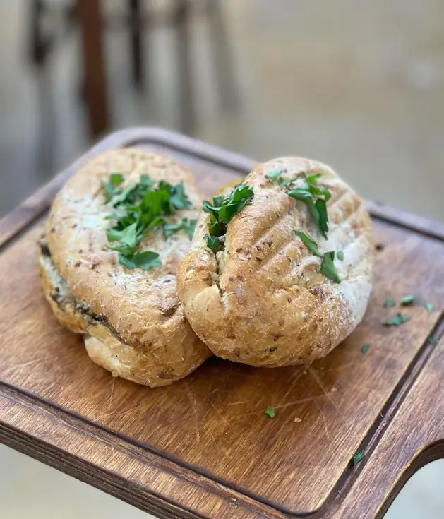 ساندویچ‌های گریل و تازه کافه گالری رحیمیه، با نان تست شده و سبزیجات معطر روی تخته چوبی، آماده سرو در محیط دلنشین.