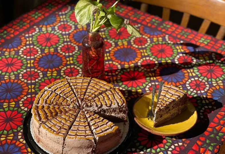 کیک شکلاتی خوشمزه با تزئین کارامل و شکلات، مناسب عصرانه در کافه گالری رحیمیه. روی رومیزی سنتی و رنگارنگ با گلدان.