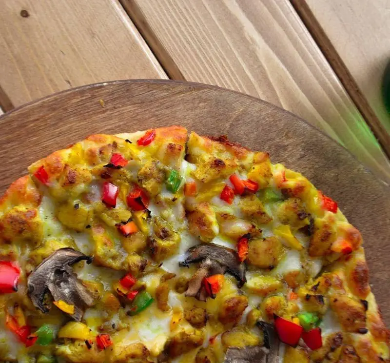 پیتزا مرغ و قارچ خوشمزه کاوان با فلفل دلمه‌ای رنگی و پنیر آب شده، روی تخته چوبی، بهترین انتخاب برای یک وعده غذایی لذیذ از فست فود کاوان.