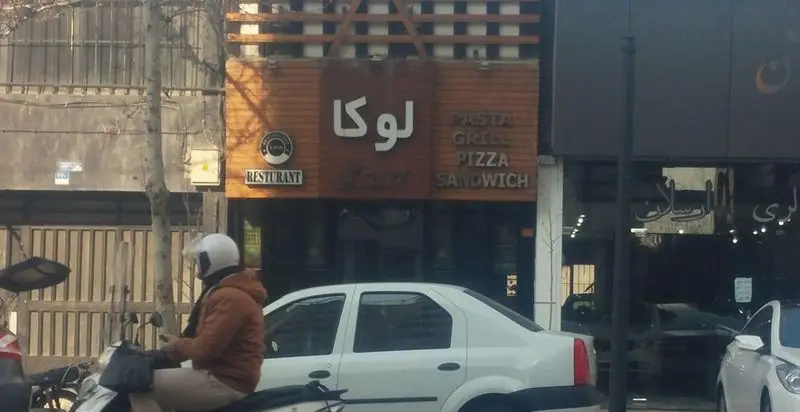 نمای بیرونی کافه رستوران لوکا، با تابلوی بزرگ «لوکا» و لیست غذاهای پاستا، گریل، پیتزا و ساندویچ در یک روز آفتابی.