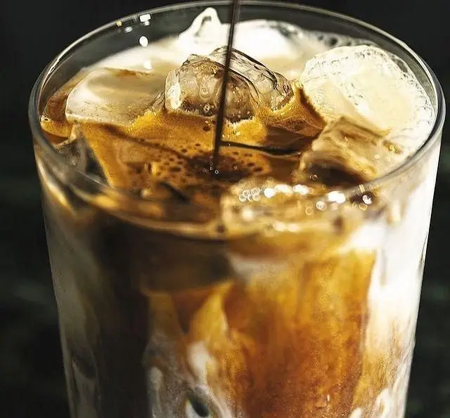 آیس کافی خنک و خوشرنگ کافه گیو؛ نمای نزدیک از لحظه ریختن قهوه روی یخ و شیر، یک نوشیدنی عالی برای تابستان گرم.