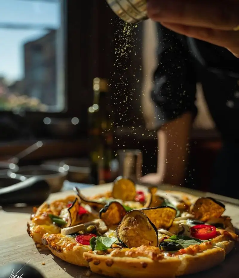 پیتزای تازه و خوشمزه کافه لیو با تاپینگ‌های سبزیجات نظیر بادمجان، قارچ و فلفل، در حال طعم‌دار شدن با پنیر. لذت یک وعده خاص.