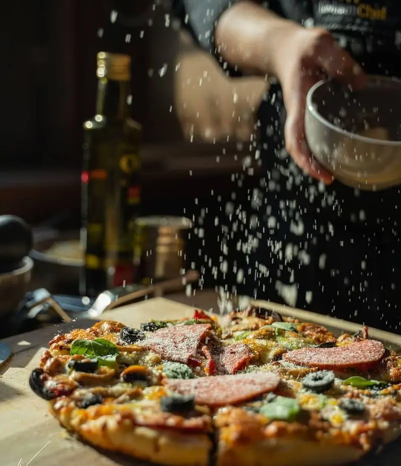 پیتزای لذیذ کافه لیو با تاپینگ سوسیس، زیتون، قارچ و سبزیجات. پاشیدن پنیر پارمزان روی پیتزا. طعم بی‌نظیر پیتزا در کافه لیو.