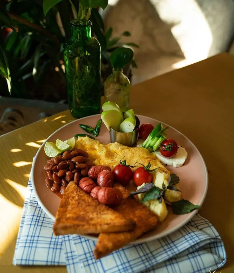 صبحانه کامل و خوشمزه کافه لیو شامل املت، سوسیس، لوبیا، نان تست و میوه تازه؛ ایده‌آل برای شروع یک روز خوب.