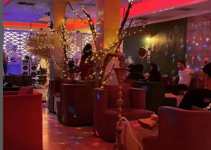 فضای داخلی چايخانه رهروان با دکوراسیون مدرن، درختان نورانی، قلیان، مشتریان در حال استراحت و نورپردازی رنگی. کافه رهروان.