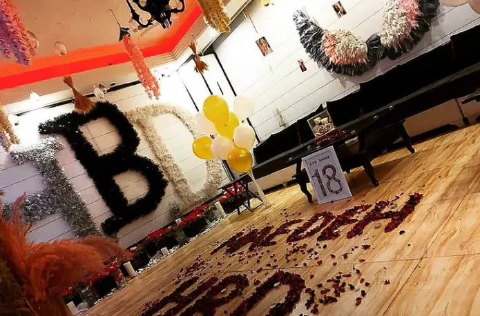 دکوراسیون شیک جشن تولد ۱۸ سالگی در فضای VIP چايخانه رهروان، شامل حروف تزئینی HBD، بادکنک‌های شاد و گلبرگ‌های رز روی زمین، میزبانی از رویدادها.