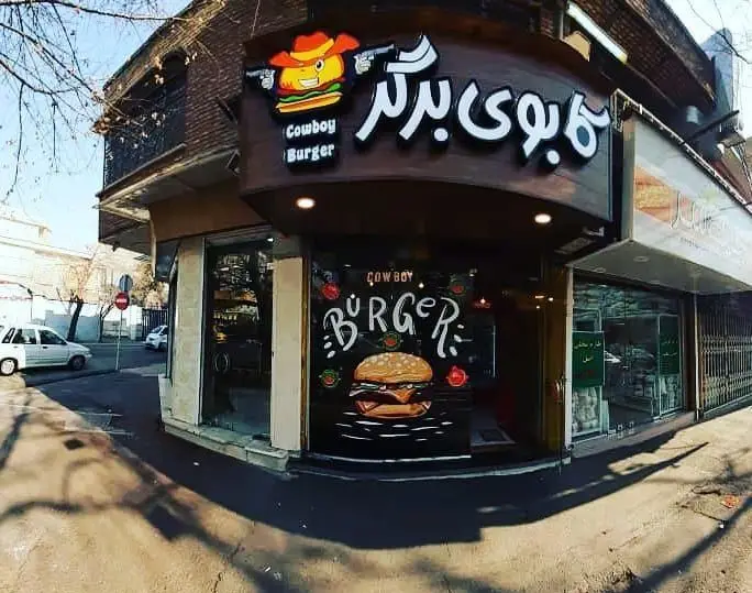 نمای بیرونی رستوران فست فود کابوی برگر در روز روشن، با تابلوی بزرگ و لوگوی برجسته کاراکتر برگر کلاه کابوی مسلح.