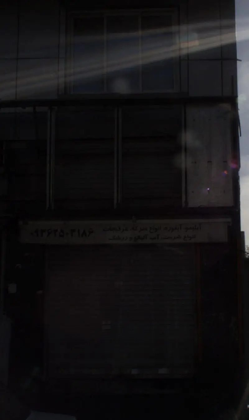 نمای تاریک و بسته فروشگاه آبمیوه و بستنی صمد، با تابلوی محصولات شامل انواع آبمیوه، عرقیجات، شربت‌ها، آب آلبالو و زرشک.