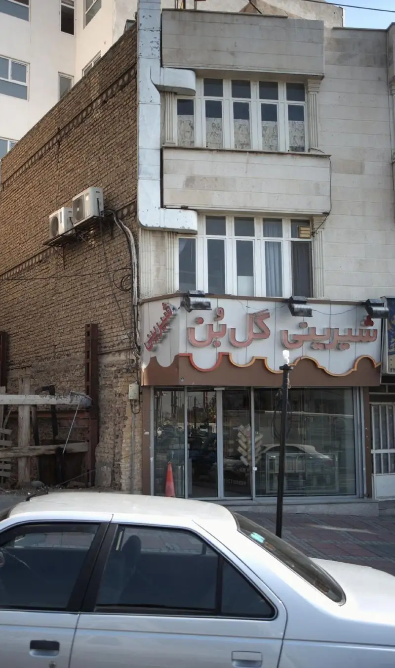 نمای بیرونی شیرینی‌فروشی و قنادی "گل بن" با تابلوی نئون، ویترین شیشه‌ای پر از محصولات و معماری آجری و سنگی ساختمان.