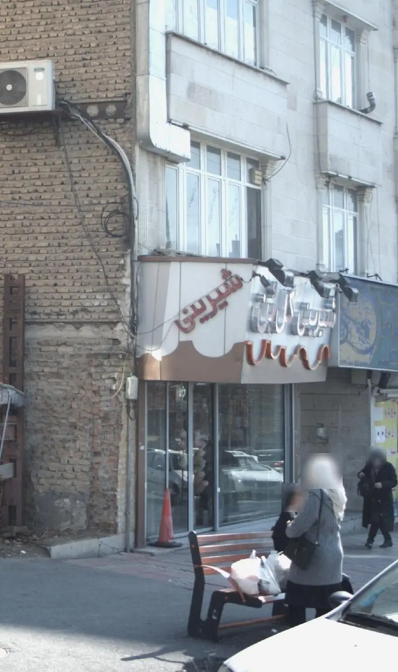 تصویر کسب و کار شیرینی گل بن، نمای بیرونی قنادی با تابلوی فارسی، ساختمان آجری و عابران پیاده در جلوی فروشگاه.