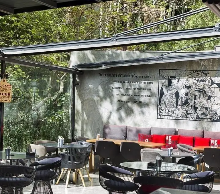 نمایی از فضای باز و دنج کافی شاپ راندوو با دکوراسیون مدرن، مبلمان راحت، و دیوار نقاشی گرنیکا، مناسب استراحت و گپ‌وگفت.