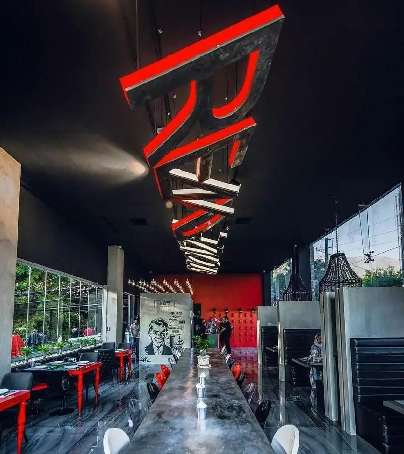 فضای داخلی مدرن و شیک کافی شاپ راندوو با نورپردازی خلاقانه، سقف بلند مشکی، میزهای بلند و نشیمنگاه راحت، و پنجره‌های بزرگ رو به فضای سبز.