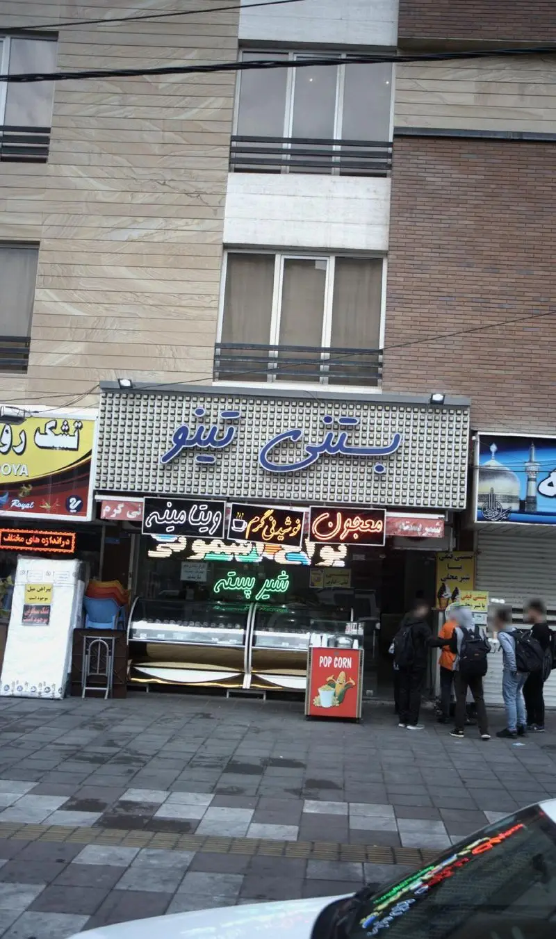 ویترین پرنور بستنی فروشی تینو با تابلوهای نئون معجون، شیر پسته، نوشیدنی گرم، ویتامینه و پاپ‌کورن در یک روز معمولی.