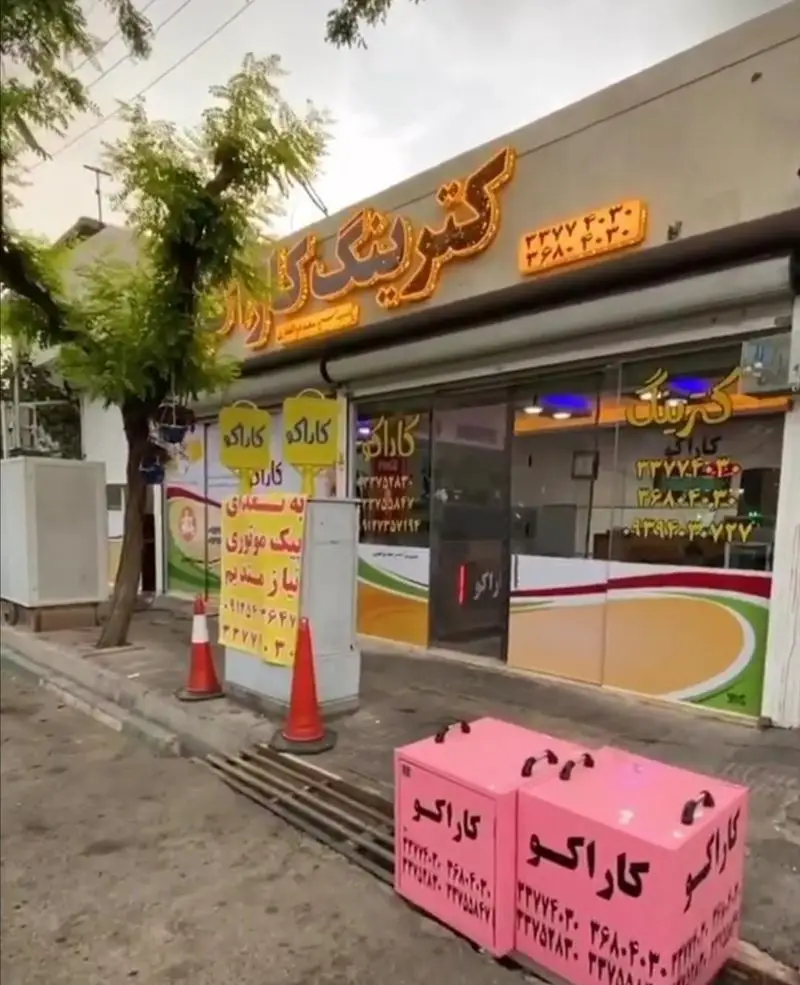 نمای فروشگاه کترینگ کاراکو با تابلو درخشان و شماره تماس‌های ۳۳۷۷۴۰۳۰ و ۲۶۸۰۴۰۳۰. جعبه‌های حمل غذا و اطلاعیه استخدام پیک.