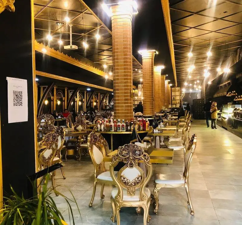 نمایی از فضای داخلی رستوران وی آی پی کاظمی با دکوراسیون مشکی و طلایی شیک، ستون‌های آجری، مبلمان سلطنتی و محیطی دلنشین.